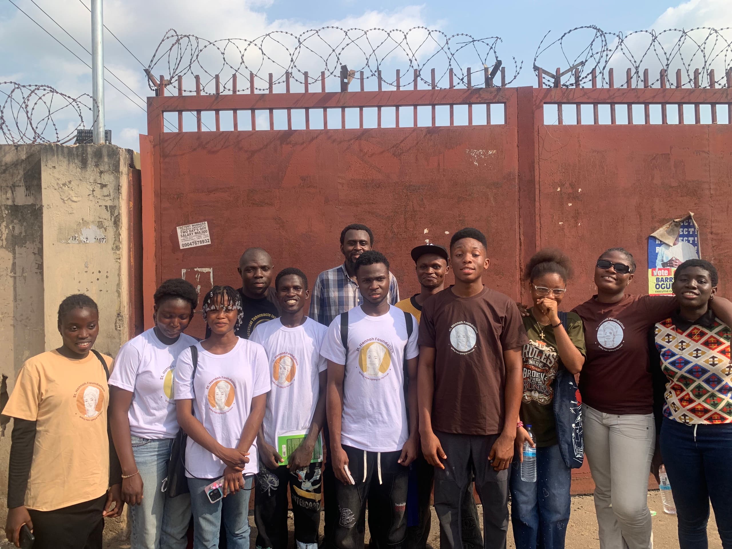 UTME students and staff stand together in front of a red gate.