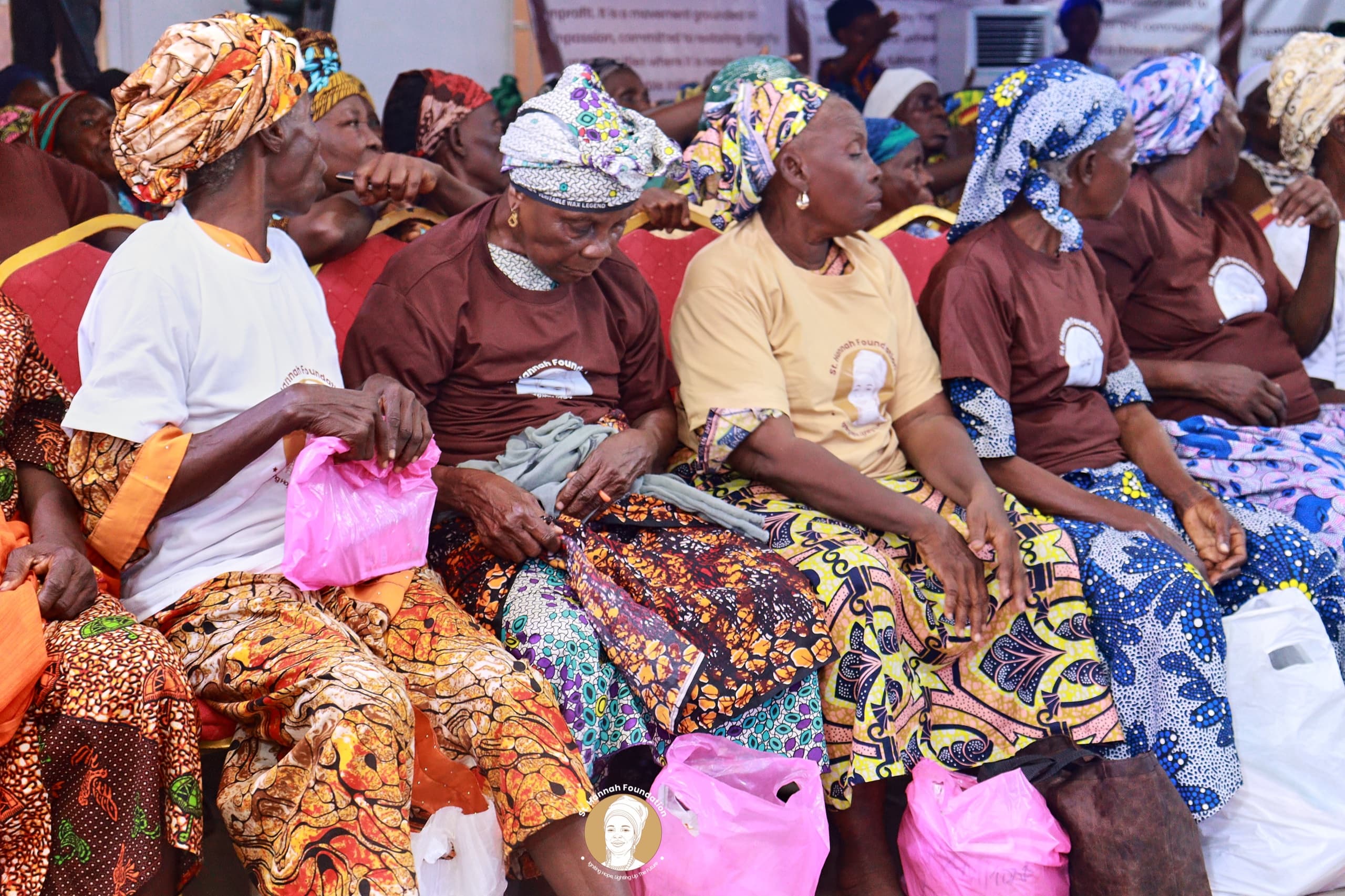 Seated widows in Foundation T-shirts hold the pink and white bags they have received.